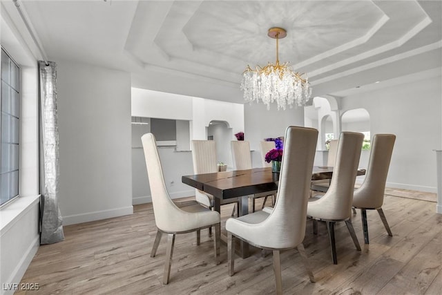 dining room featuring light wood-type flooring, an inviting chandelier, a wealth of natural light, and a raised ceiling