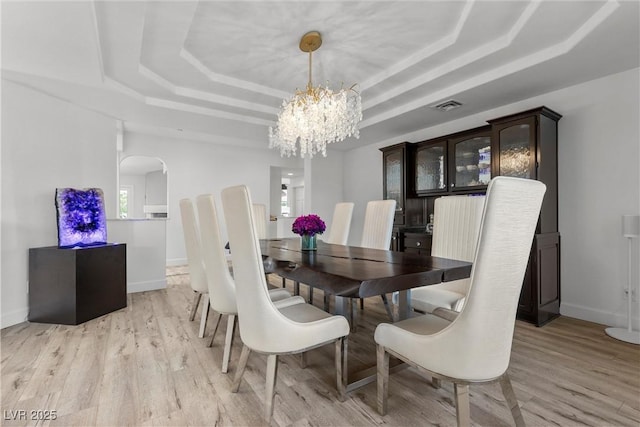 dining space featuring light hardwood / wood-style floors, a raised ceiling, and a chandelier