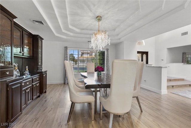 dining space with a raised ceiling, a notable chandelier, and light wood-type flooring