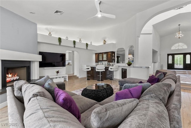 living room with ceiling fan with notable chandelier, light hardwood / wood-style flooring, and lofted ceiling