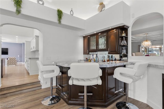 bar with decorative backsplash, dark brown cabinetry, light hardwood / wood-style flooring, and a notable chandelier