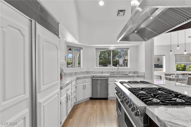 kitchen featuring wall chimney range hood, light stone countertops, high quality appliances, white cabinets, and sink