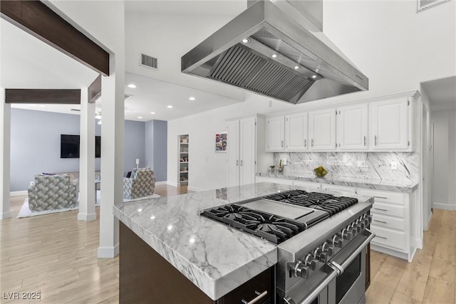 kitchen featuring high end stainless steel range, white cabinetry, tasteful backsplash, island range hood, and light stone counters