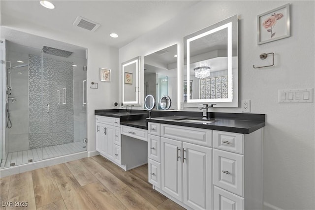 bathroom featuring an inviting chandelier, a shower with shower door, wood-type flooring, and vanity