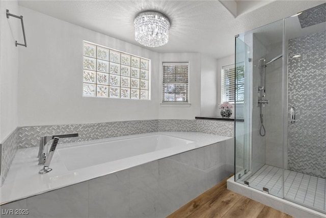 bathroom with an inviting chandelier, shower with separate bathtub, and hardwood / wood-style flooring