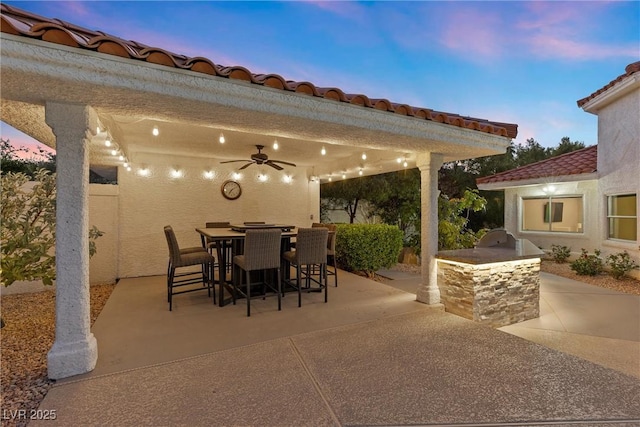 patio terrace at dusk featuring ceiling fan and area for grilling