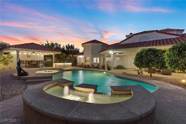 pool at dusk with pool water feature, a patio area, an in ground hot tub, and an outdoor bar