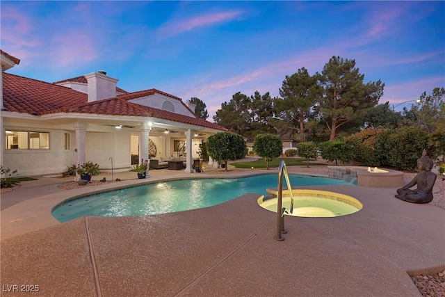 pool at dusk featuring ceiling fan, an outdoor hangout area, a patio, and an in ground hot tub