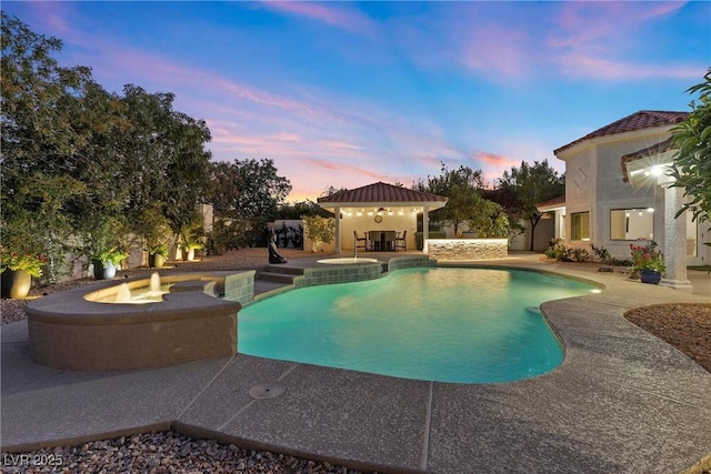 pool at dusk featuring a patio area and an in ground hot tub