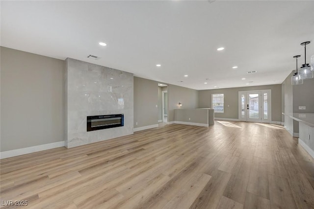 unfurnished living room featuring light wood-type flooring, a fireplace, and french doors