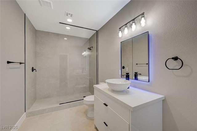 bathroom featuring toilet, vanity, tile patterned floors, and tiled shower