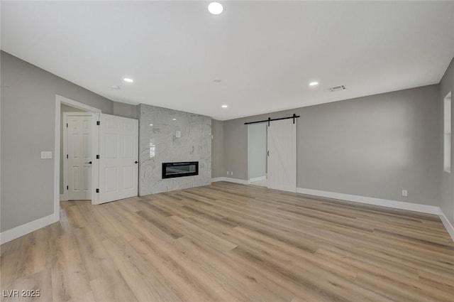 unfurnished living room with a barn door, light wood-type flooring, and a fireplace