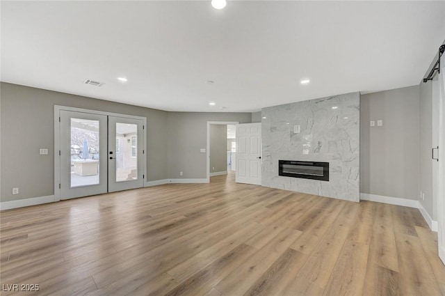 unfurnished living room featuring light wood-type flooring, french doors, and a fireplace