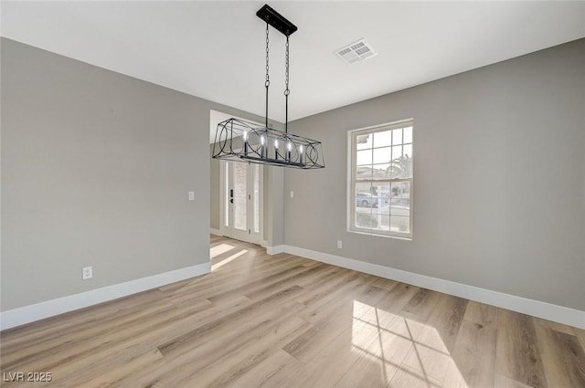 unfurnished dining area featuring an inviting chandelier and light hardwood / wood-style flooring