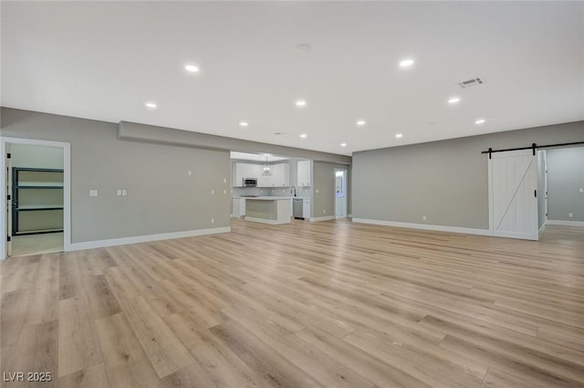 unfurnished living room with light hardwood / wood-style floors and a barn door