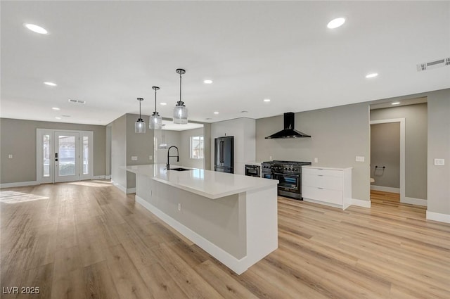 kitchen with double oven range, a spacious island, black fridge, wall chimney range hood, and sink