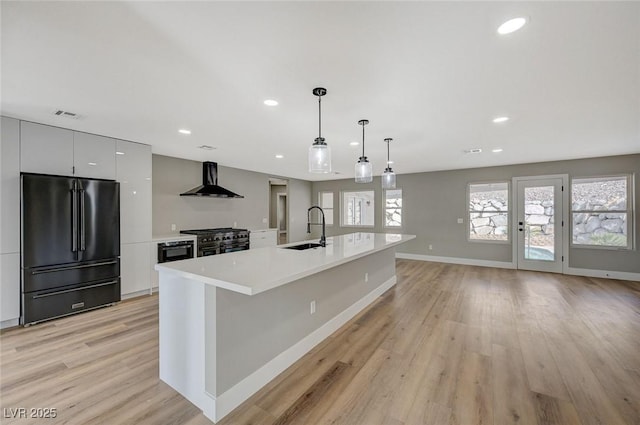 kitchen with black appliances, wall chimney range hood, sink, hanging light fixtures, and a large island