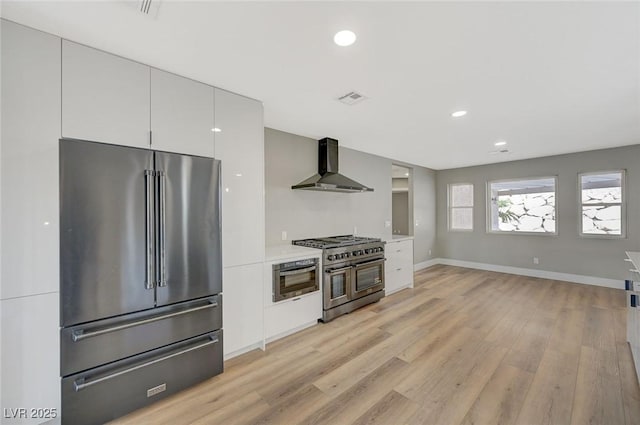 kitchen featuring light hardwood / wood-style floors, premium appliances, white cabinets, and wall chimney exhaust hood