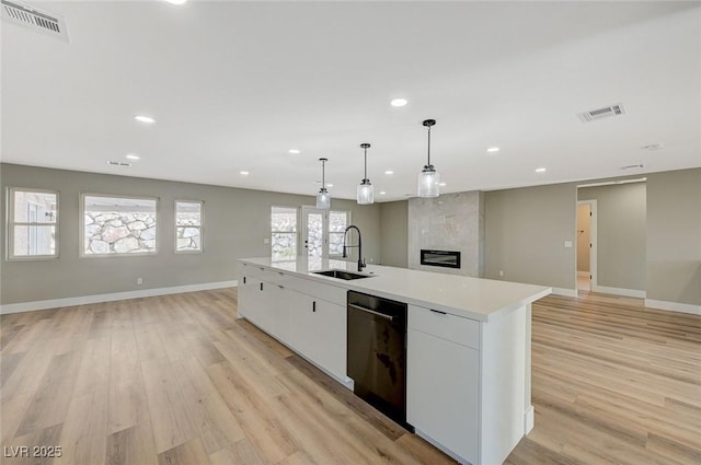 kitchen with decorative light fixtures, dishwasher, sink, white cabinetry, and a kitchen island with sink