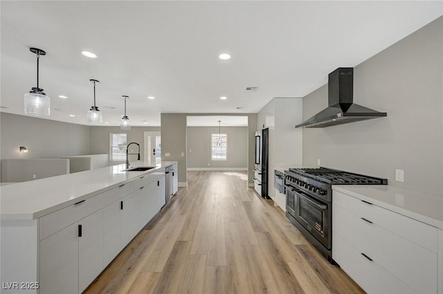 kitchen with light hardwood / wood-style floors, decorative light fixtures, range with two ovens, wall chimney exhaust hood, and sink