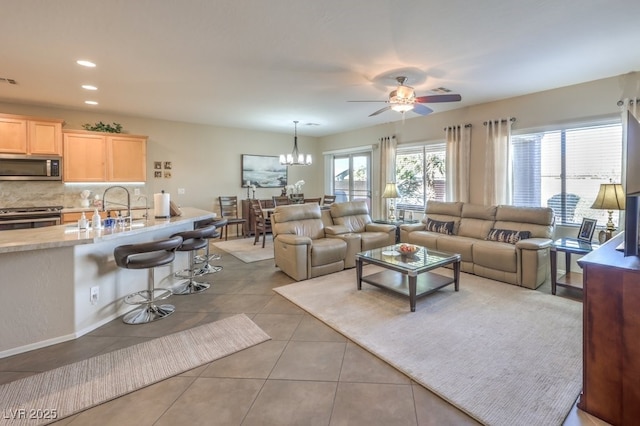 living room with light tile patterned flooring, ceiling fan with notable chandelier, and sink