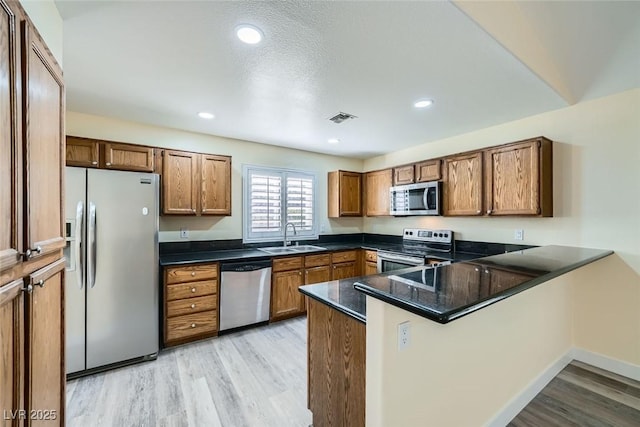 kitchen featuring kitchen peninsula, appliances with stainless steel finishes, a textured ceiling, light hardwood / wood-style flooring, and sink