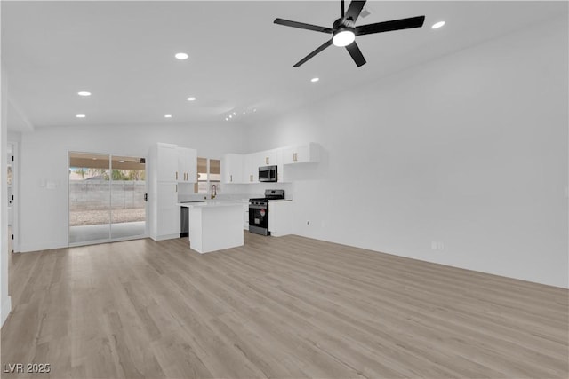 unfurnished living room featuring ceiling fan, light wood-type flooring, sink, and high vaulted ceiling