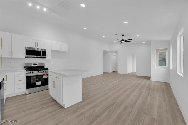 kitchen featuring appliances with stainless steel finishes, a center island, white cabinetry, light wood-type flooring, and ceiling fan