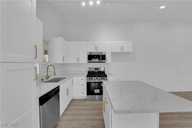 kitchen featuring appliances with stainless steel finishes, white cabinets, a kitchen island, light stone counters, and sink