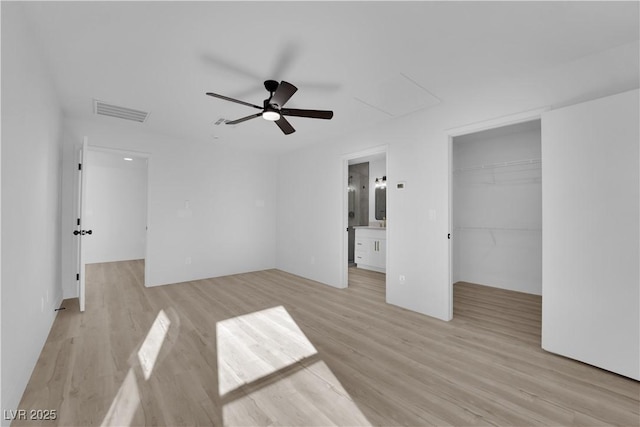 unfurnished bedroom with ceiling fan, connected bathroom, light wood-type flooring, a closet, and a walk in closet