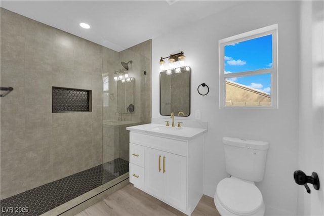 bathroom featuring toilet, a tile shower, hardwood / wood-style flooring, and vanity