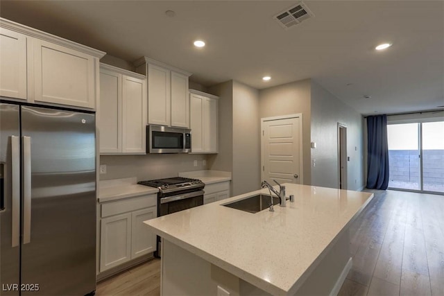 kitchen featuring stainless steel appliances, a kitchen island with sink, white cabinets, light hardwood / wood-style flooring, and sink