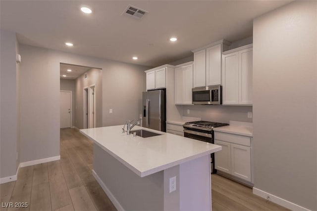 kitchen featuring white cabinetry, stainless steel appliances, light hardwood / wood-style floors, sink, and a center island with sink