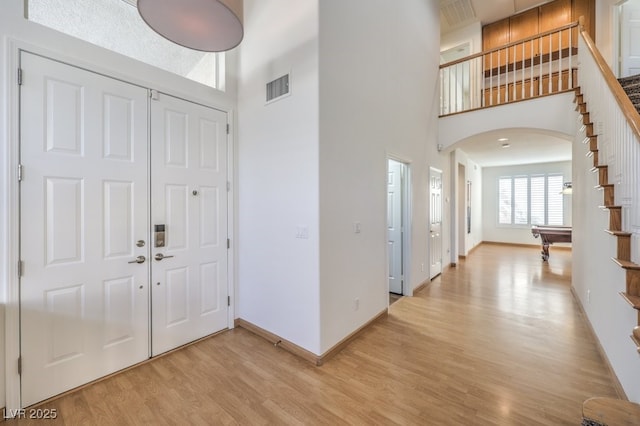 entrance foyer featuring arched walkways, light wood finished floors, visible vents, a high ceiling, and stairs