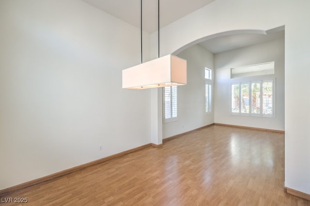 unfurnished room with light wood-type flooring, baseboards, a towering ceiling, and arched walkways