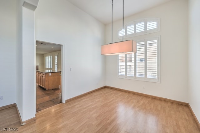 empty room with high vaulted ceiling, light wood-style flooring, and baseboards