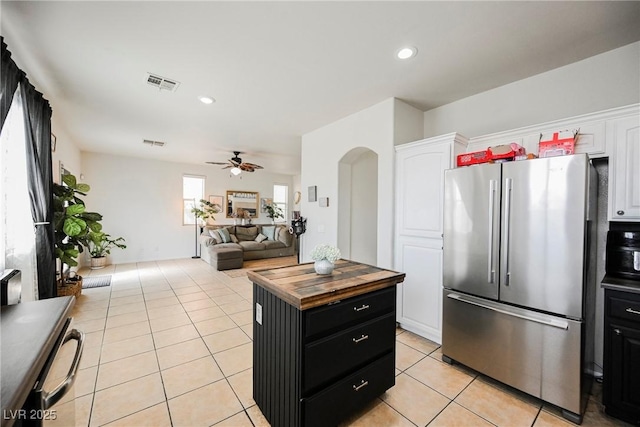 kitchen featuring ceiling fan, light tile patterned flooring, stainless steel refrigerator, white cabinets, and a center island