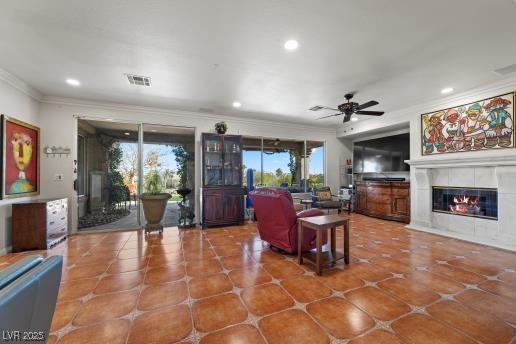 tiled living room with ceiling fan, ornamental molding, and a fireplace