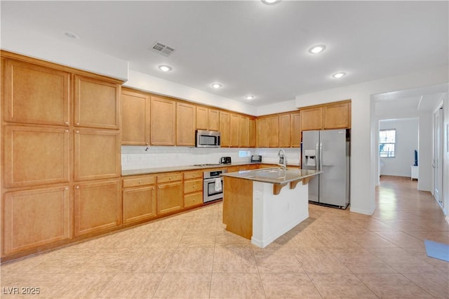 kitchen featuring a breakfast bar area, stainless steel appliances, decorative backsplash, a kitchen island with sink, and sink