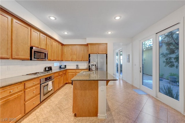 kitchen with decorative backsplash, a kitchen island with sink, appliances with stainless steel finishes, a breakfast bar area, and light stone counters