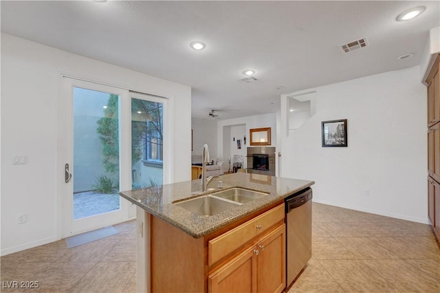 kitchen featuring sink, stainless steel dishwasher, a kitchen island with sink, and stone counters