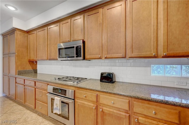 kitchen featuring light stone countertops, appliances with stainless steel finishes, light tile patterned flooring, and tasteful backsplash