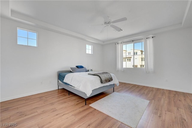 bedroom with ceiling fan, a raised ceiling, and light wood-type flooring