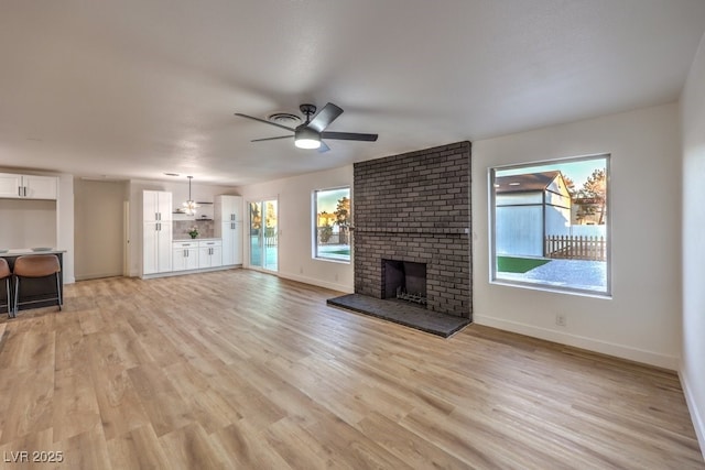 unfurnished living room with ceiling fan with notable chandelier, light hardwood / wood-style flooring, a healthy amount of sunlight, and a fireplace