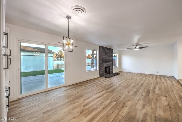 unfurnished living room with ceiling fan with notable chandelier, light hardwood / wood-style flooring, and a fireplace