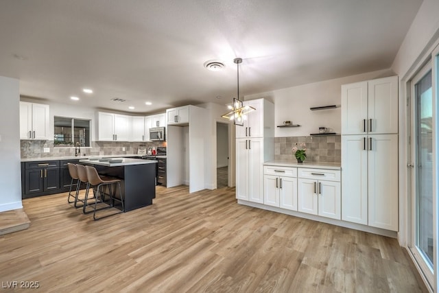 kitchen featuring decorative light fixtures, light hardwood / wood-style floors, a center island, a breakfast bar, and white cabinetry