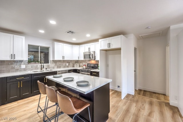 kitchen featuring a kitchen island, a breakfast bar, sink, stainless steel appliances, and white cabinets