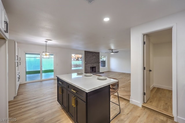 kitchen with a center island, decorative light fixtures, ceiling fan, a brick fireplace, and a breakfast bar area