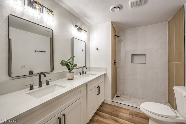 bathroom featuring toilet, vanity, tiled shower, hardwood / wood-style flooring, and a textured ceiling