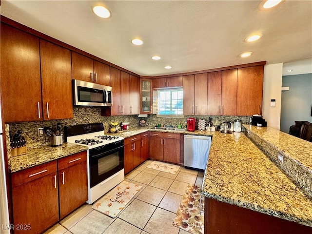 kitchen with kitchen peninsula, sink, light stone countertops, appliances with stainless steel finishes, and light tile patterned floors